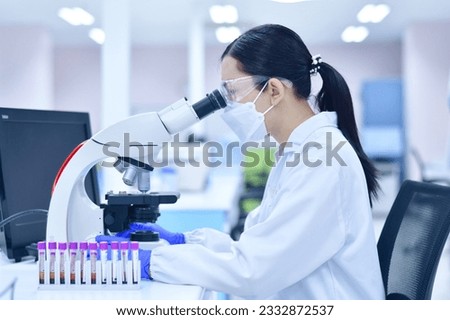 Female medical technologist looking at slides on microscope for diagnosis in laboratory. Royalty-Free Stock Photo #2332872537