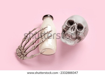 Bottle of milk, skull and skeleton hand for Halloween on pink background, closeup