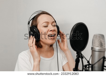 young beautiful caucasian woman singing song with smile in black microphone in sound record studio in white room for distributing music and becoming recognizable and popular, music record concept