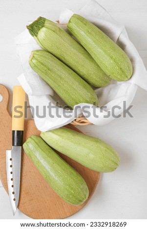 Bowl and board with fresh green zucchini on white wooden background Royalty-Free Stock Photo #2332918269