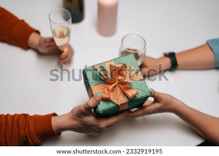 Close-up top view of woman giving box with gift to man sitting at table with candles on birthday or Valentines Day. Happy boyfriend receiving present from wife enjoying romantic dinner date.