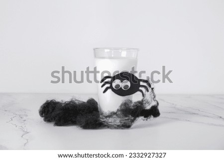 Glass of milk and spider made of paper for Halloween on light background