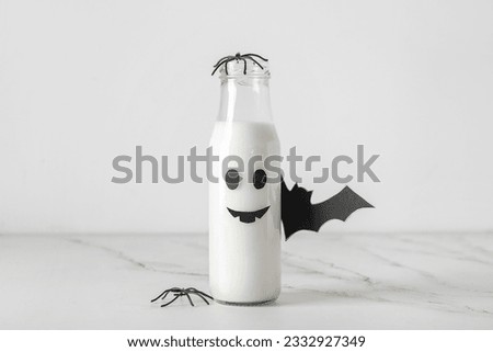 Bottle of milk, spider and bat made of paper for Halloween on light background