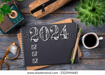 New year resolutions 2024 on desk. 2024 goals list with notebook, coffee cup, plant on wooden table. Resolutions, plan, goals, action, checklist, idea concept. New Year 2024 resolutions, copy space Royalty-Free Stock Photo #2332944685