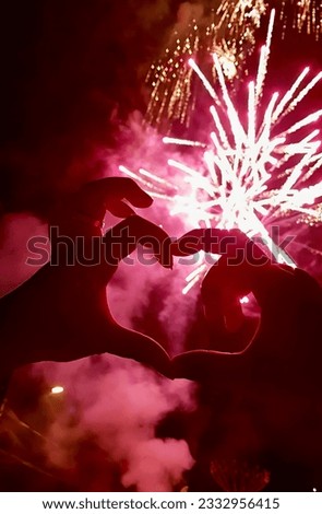 a photography of a person making a heart shape with their hands, someone making a heart shape with their hands with fireworks in the background.