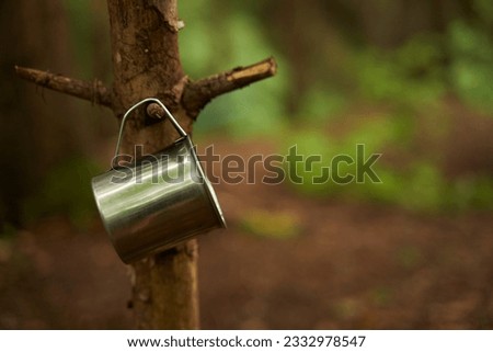 A metal tourist mug hangs on a tree. Empty space for text. 