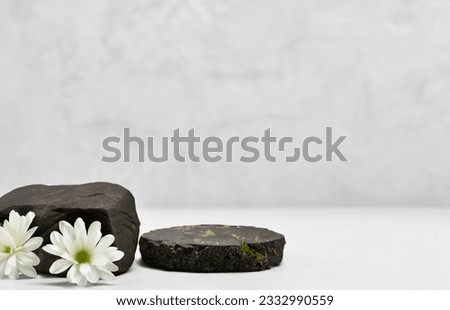 Background for cosmetic products. Black stone podium with white flowers. Product display stand. Front view.
