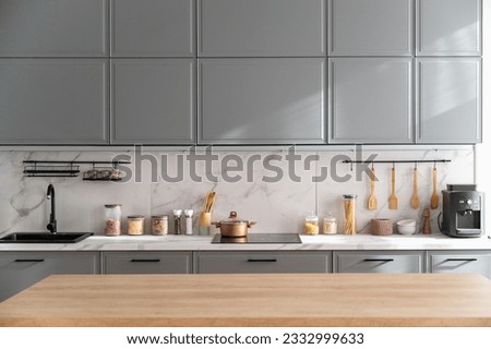 Empty wooden tabletop in scandinavian style kitchen with gray furniture. Countertop with various jars and tableware in apartment with minimalist bright interior.