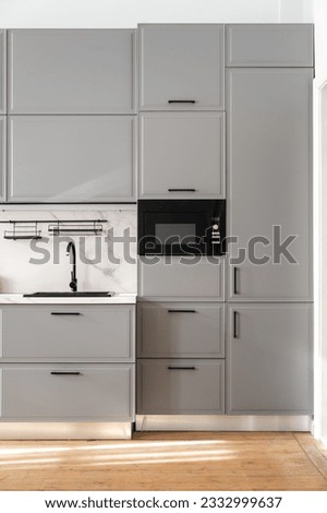 Vertical shot of gray minimalist cupboard with built-in appliance and kitchen furniture on wooden floor. Scandinavian style in modern home interior. Monochrome design with marble countertop Royalty-Free Stock Photo #2332999637