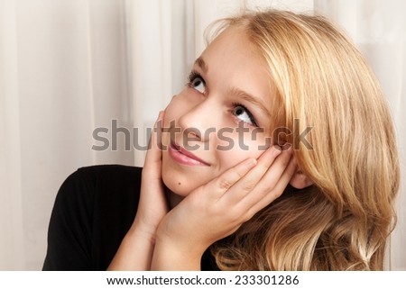 Beautiful blond Caucasian girl is looking up with smile, closeup studio portrait