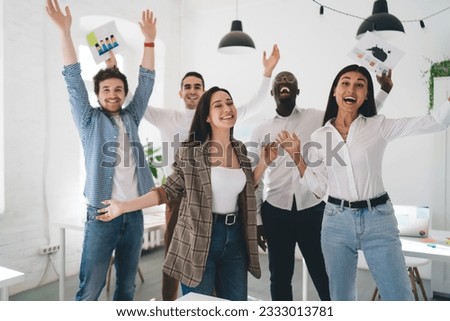 Group of happy multiethnic employees screaming dancing and raising arms celebrating victory throwing papers in air in light creative office Royalty-Free Stock Photo #2333013781