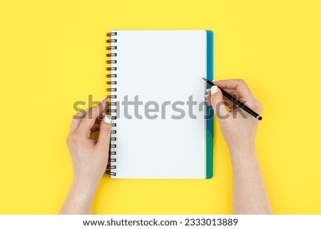Female hands writing in notepad on yellow background, flat lay.