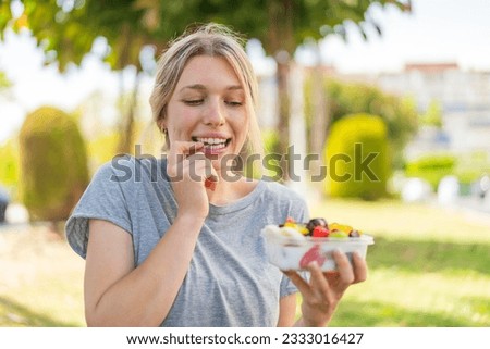 Young blonde woman holding a bowl of fruit at outdoors