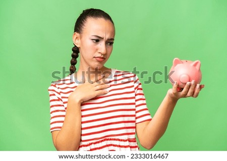 Young Arab woman holding a piggybank over isolated background with sad expression