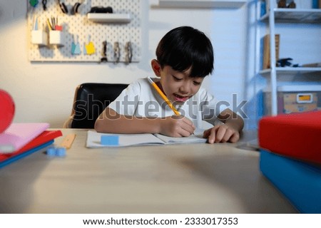 Asian Kid Boy Happiness Focused on Homework and Learning Alone in Room at Home, Serious Asian Kid Concentrating on Homework, Studying and Success, Homework and Education of Asian Kids Concept. Royalty-Free Stock Photo #2333017353
