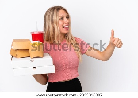 Young caucasian woman holding fat food isolated on blue background giving a thumbs up gesture