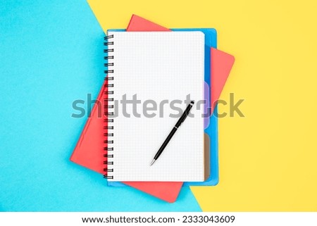 Notebooks and pen on a blue and yellow background, top view.