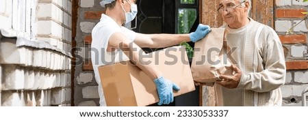 An elderly woman using a walker receives meals from a man working with a benevolent group delivering food to those who are at high risk because of the coronavirus COVID19. Royalty-Free Stock Photo #2333053337