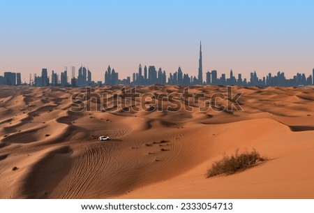 Dubai skyline on the horizon of a sand and dune landscape with tire tracks from a 4x4 vehicle during safari excursion. Blue sky at sunset.