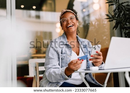Happy woman sitting in a café and using her smartphone for online shopping, paying with a credit card. Young woman enjoying the convenience of mobile banking and digital transactions. Royalty-Free Stock Photo #2333077665