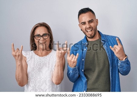 Hispanic mother and son standing together shouting with crazy expression doing rock symbol with hands up. music star. heavy music concept.  Royalty-Free Stock Photo #2333088695