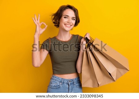 Photo of excited shiny lady wear khaki t-shirt rising shoppers showing okey gesture isolated yellow color background