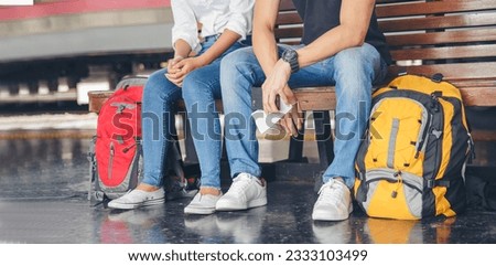 banner-Cheap Travel and Lifestyle concept. Young Traveler man and woman (Couple of Love) wearing sneaker and sitting at train station. Asian Backpacker waiting train and plan trip with smartphone.