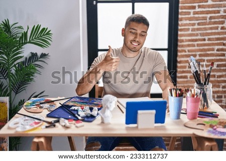 Young hispanic painter man doing online call with tablet smiling happy and positive, thumb up doing excellent and approval sign 