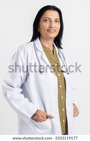 Portrait of smiling confident mature female doctor wearing lab coat standing against white background.