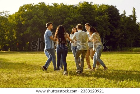 Happy cheerful friends are having fun in the park in summer. Group of joyful young diverse people are enjoying summertime, dancing a round dance and having a good time together