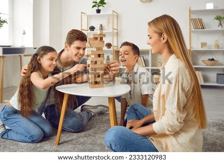 Happy family playing Jenga board game together at home. Mom, dad and their two children sitting on floor at coffee table spending free time together in living room. Family indoor activities