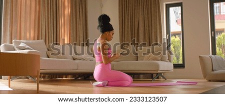 Young African American sporty young woman preparing for a workout in the living room at home, using yoga online fitness training application to get the sports plan