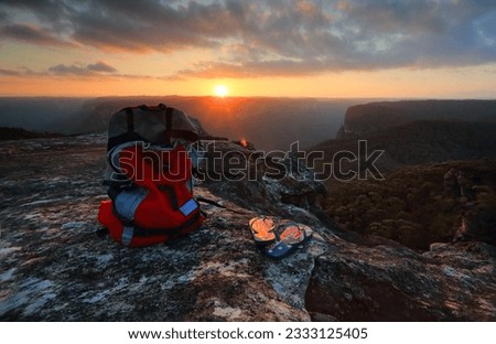 Sunset from a rocky outcrop of the Explorers Range, Blue Mountains Australia. A backpack and thongs with Australian flag sit catch the last light of the setting sun pver the Pierces Pass and Govets