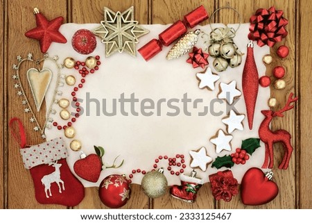 Christmas background border with bauble decorations, star shaped gingerbread biscuits, holly and mistletoe on parchment paper on distressed wood.