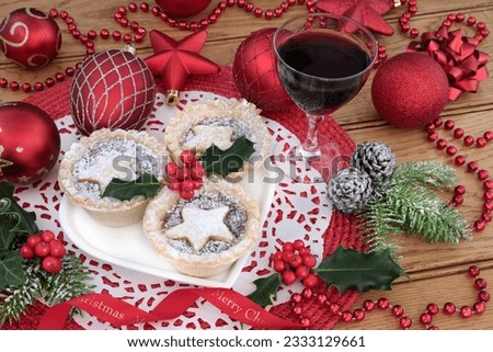 Christmas mince pie cakes on a heart shaped plate with dessert wine, holly, fir and red bauble decorations on a place mat on oak table background.