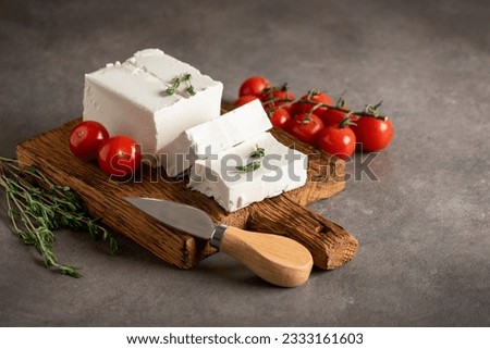 Feta cheese on a wooden board with thyme and cherry tomatoes. Brown rustic background. Side view, selective focus.