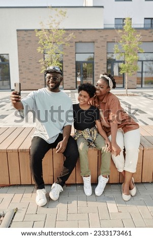 Vertical image of happy African American family making selfie portrait on smartphone in the city