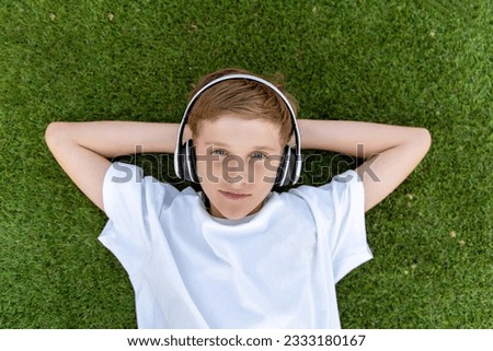 boy with headphones listening to music lying on the grass in the park looking at the camera