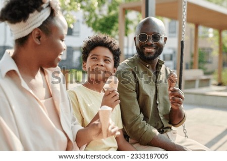 Happy African American family eating ice cream together outdoors while sitting on the swing Royalty-Free Stock Photo #2333187005