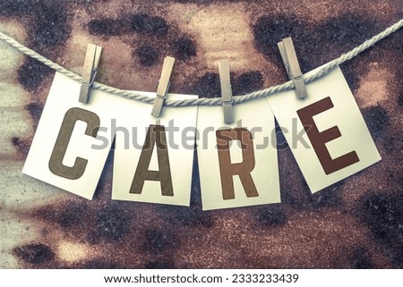 The word -CARE- stamped on cards and pinned to an old piece of twine over a rusted metal background.