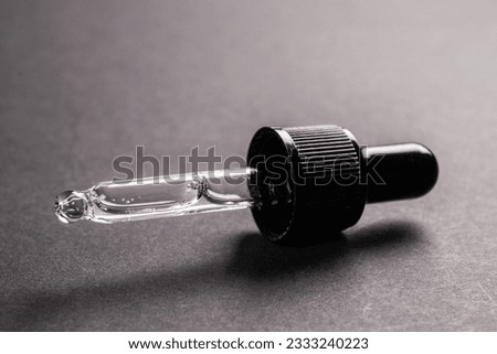 cosmetic pipette with a drop close up on dark background.