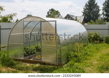 Transparent semicircular polycarbonate greenhouse close-up in the garden on a summer day Royalty-Free Stock Photo #2333245089