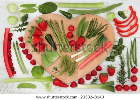 Health food with red and green vegetable and fruit selection on a heart shaped board over distressed white wood background. High in vitamins, antioxidants, minerals and anthocyanins.
