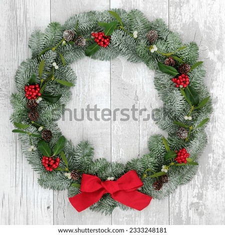 Traditional christmas wreath decoartion with holly, fir and mistletoe over distressed white wood front door background.