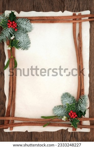 Christmas abstract background border with cinnamon sticks, holly, ivy, mistletoe and snow covered fir on parchment paper over oak wood.