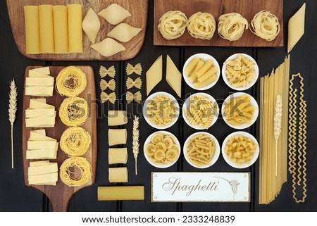 Dried italian pasta food selection on maple boards and in porcelain bowls with old spaghetti sign forming an abstract background over dark wood.