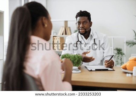 Confident man with stethoscope writing on paper clipboard during conversation with multiracial woman in office. Serious nutrition expert making notes of patient's medical history for proper meal plan. Royalty-Free Stock Photo #2333253203