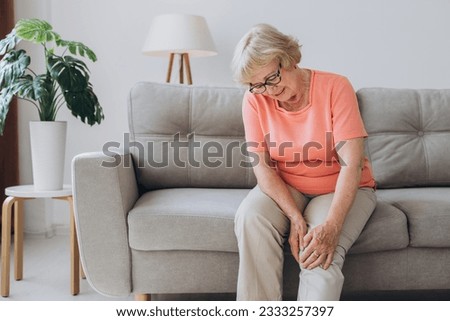 Senior woman suffering from pain in knee at home Royalty-Free Stock Photo #2333257397