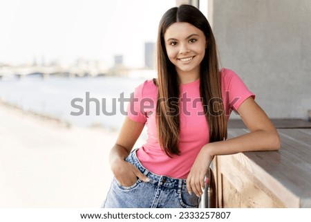 Authentic portrait of cute smiling teenage girl wearing stylish ping t shirt looking at camera standing on the street. Young attractive fashion model posing for pictures outdoors. Summer concept 