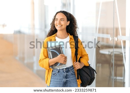 Woman university student. Happy lovely brazilian or hispanic female student, with a backpack, hold books and notebooks in her hand, stand near the university campus, looks and smile to the side